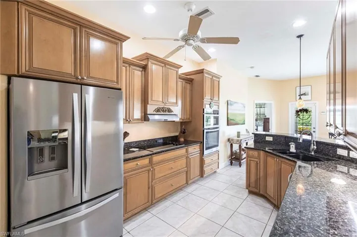 Kitchen with stainless steel appliances, light tile patterned floors, decorative light fixtures, brown cabinets, and a ceiling fan