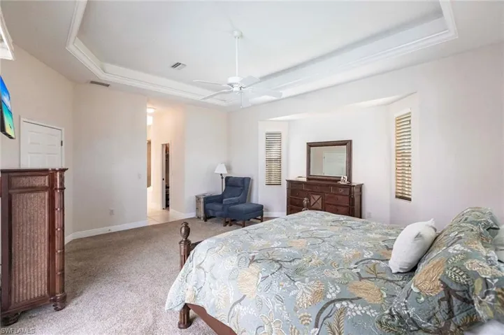 Carpeted bedroom with a raised ceiling and a ceiling fan