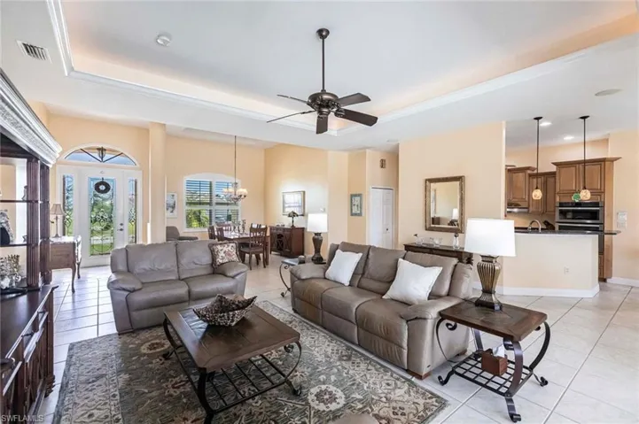Living room with a raised ceiling, a ceiling fan, light tile patterned floors, a chandelier, and recessed lighting