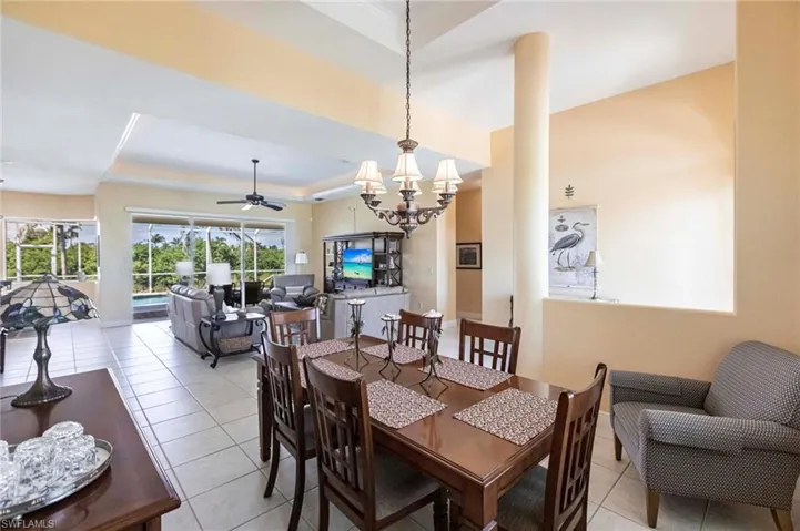 Dining area featuring a raised ceiling, light tile patterned flooring, a chandelier, and ceiling fan