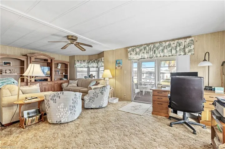 Office space featuring light colored carpet, wooden walls, and ceiling fan