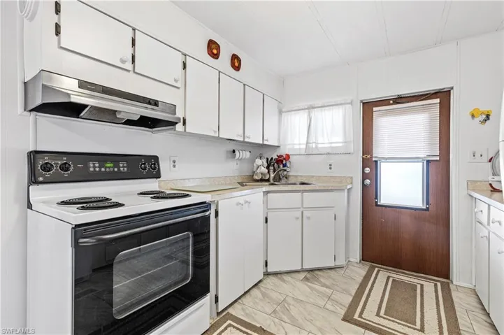 Kitchen with electric range oven, white cabinets, light countertops, and under cabinet range hood