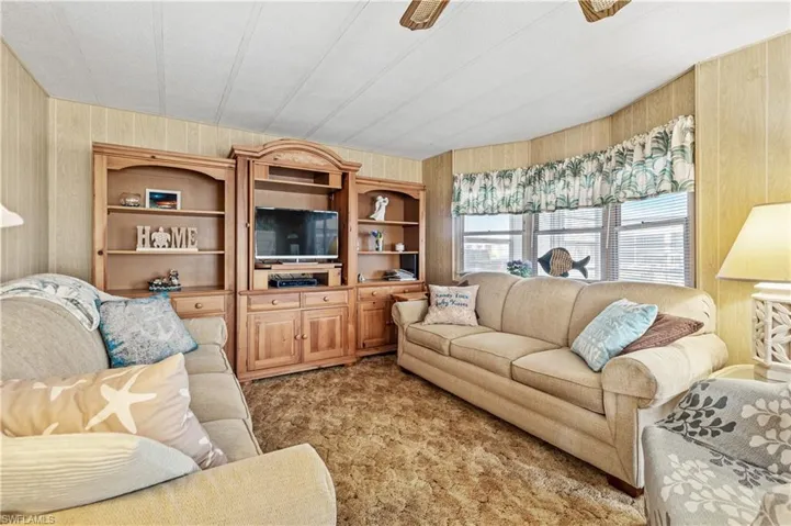 Living area with wooden walls, light carpet, and ceiling fan