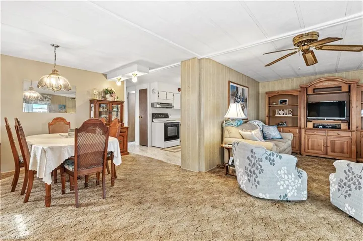 Dining room with a ceiling fan, wood walls, light carpet, and a chandelier