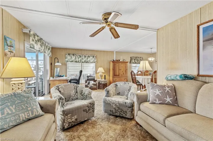Living area featuring wooden walls, ceiling fan, carpet flooring, and an office area