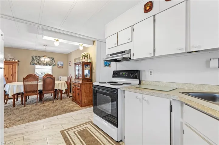 Kitchen with white range with electric cooktop, white cabinetry, light countertops, pendant lighting, and under cabinet range hood