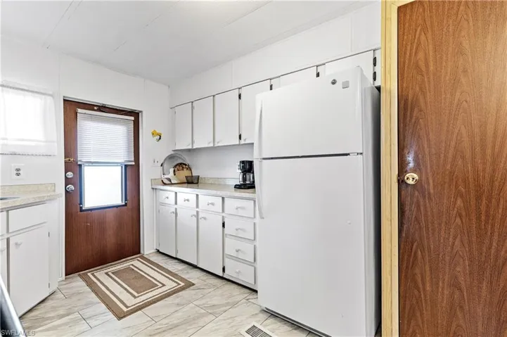 Kitchen with freestanding refrigerator, white cabinets, light countertops, and light marble finish flooring