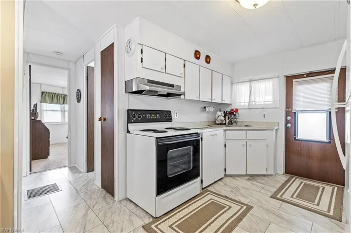 Kitchen with white range with electric stovetop, white cabinets, light countertops, light marble finish flooring, and extractor fan