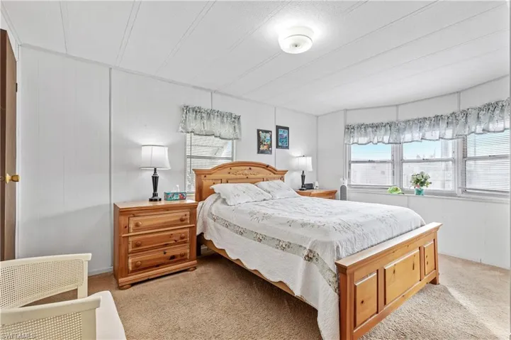Bedroom with light carpet, multiple windows, wood walls, and a decorative wall