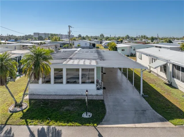 View of front of house featuring a front lawn, a residential view, an attached carport, concrete driveway, and a metal roof