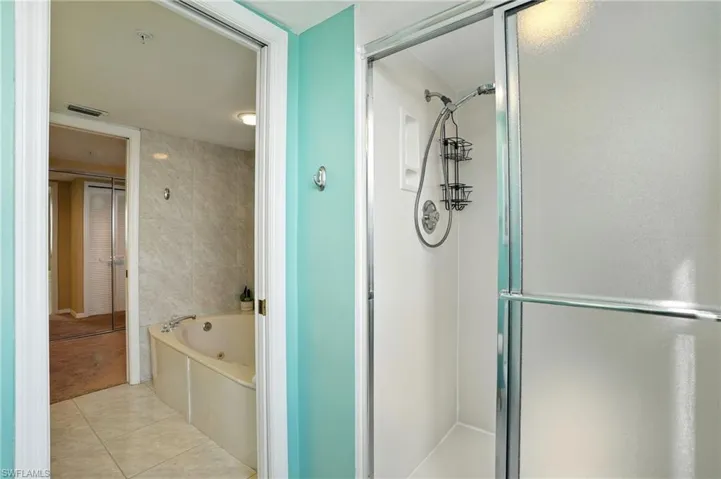 Bathroom featuring an enclosed shower, a jetted tub, tile patterned floors, and tile walls - Virtually Edited Image