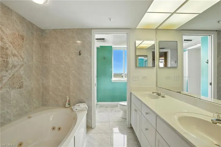 Full bath featuring a jetted tub, tile patterned flooring, double vanity, and tile walls - Virtually Edited Image