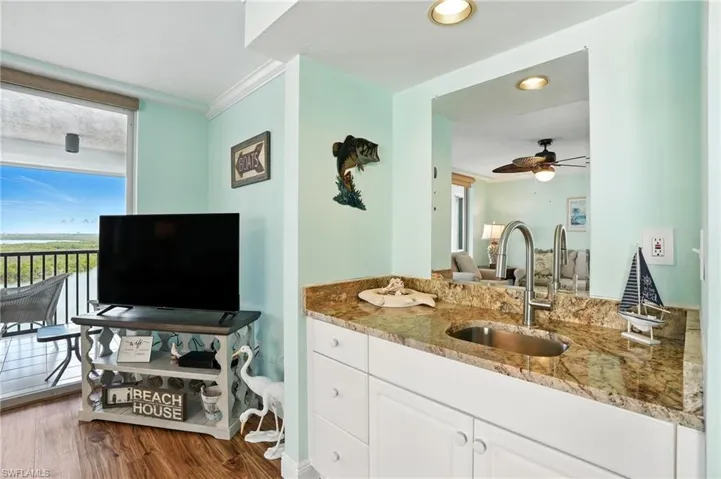 Living room featuring wet bar with wood grain floors, and crown molding - Virtually Edited Image