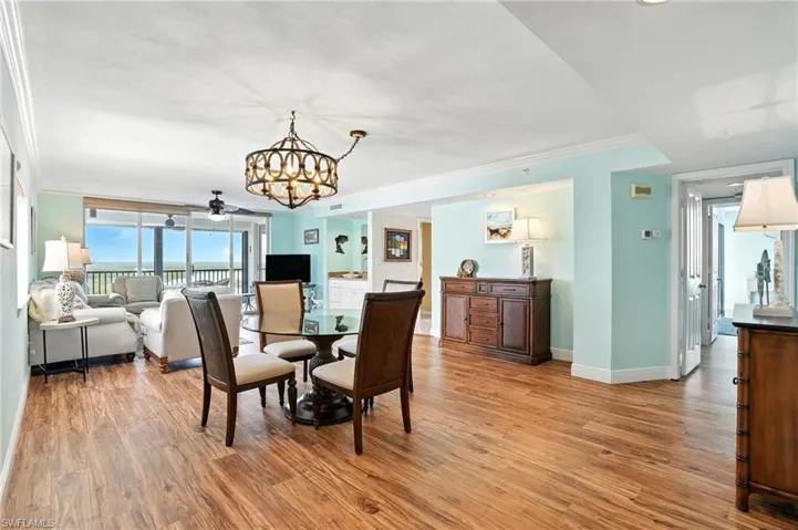 Dining area with crown molding, a chandelier, light wood finished floors, and a ceiling fan - Virtually Edited Image