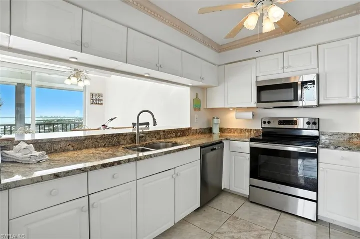 Kitchen featuring a ceiling fan, stainless steel appliances, and white cabinetry - Virtually Edited Image