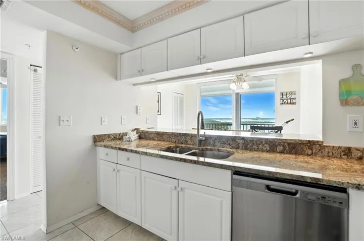 Kitchen featuring stainless steel dishwasher, stone countertops, white cabinets, and light tile patterned floors - Virtually Edited Image
