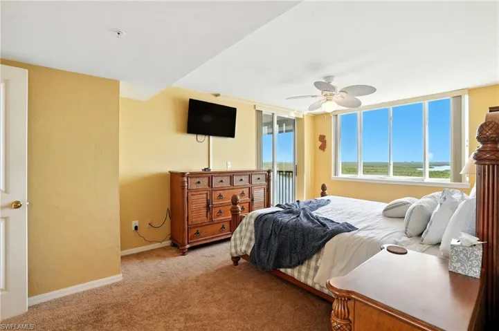 Bedroom with access to outside patio, light carpet, ceiling fan, and a textured wall with a water view - Virtually Edited Image