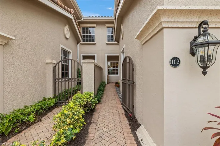 Outside is broad driveway to 2 car garage, paver entry behind gate
