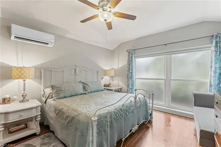 Bedroom with wood finished floors, lofted ceiling, a wall mounted air conditioner, and a ceiling fan