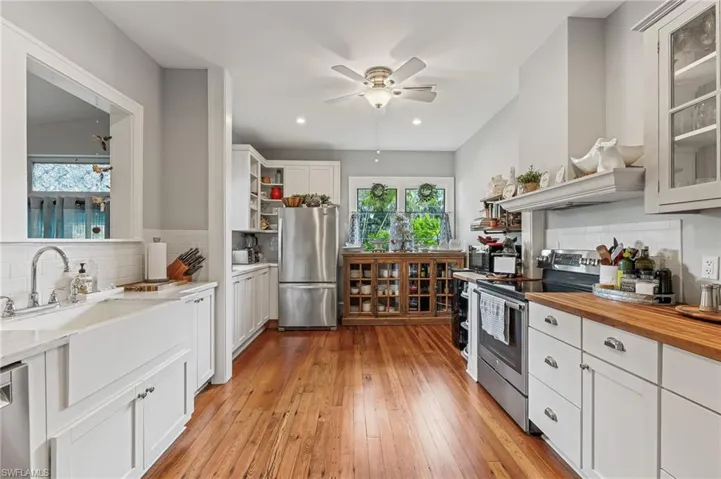 Kitchen featuring decorative backsplash, glass insert cabinets, white cabinets, appliances with stainless steel finishes, and light wood-type flooring