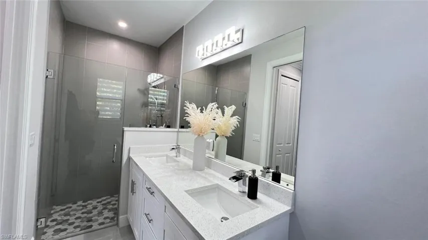 Full bath with a shower stall, double vanity, and a closet