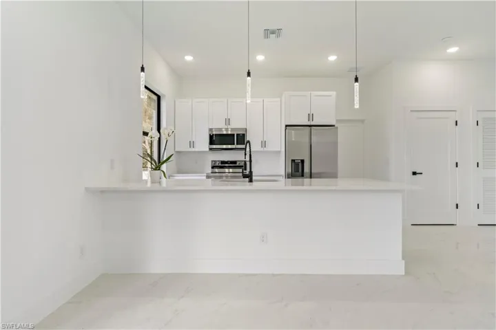 Kitchen with kitchen peninsula, appliances with stainless steel finishes, sink, white cabinetry, and hanging light fixtures