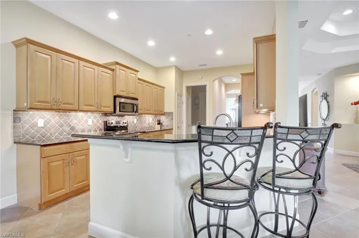 Kitchen featuring appliances with stainless steel finishes, kitchen peninsula, backsplash, light tile flooring, and a kitchen bar
