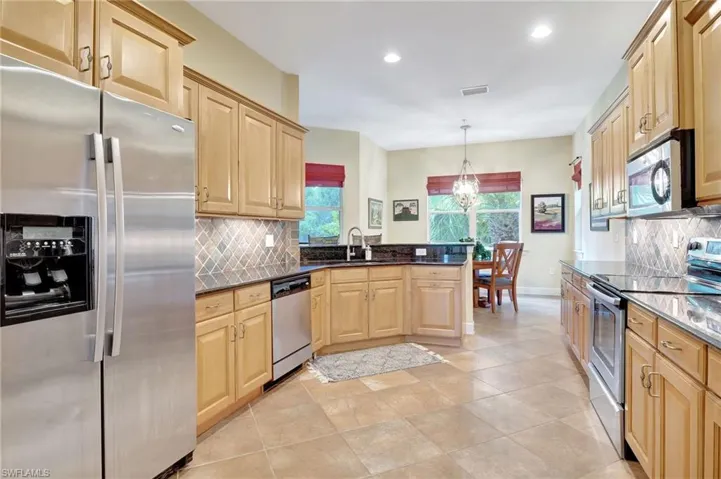 Kitchen featuring light brown cabinetry, backsplash, light tile floors, sink, and appliances with stainless steel finishes