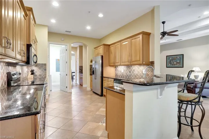 Kitchen with a kitchen breakfast bar, dark stone countertops, stainless steel appliances, kitchen peninsula, and tasteful backsplash