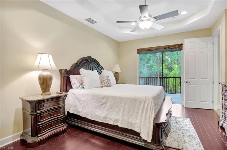 Bedroom with dark hardwood / wood-style flooring, access to exterior, ceiling fan, and a raised ceiling
