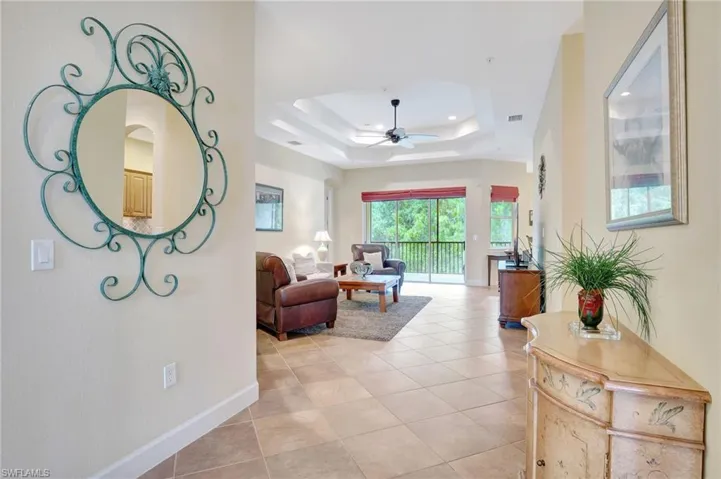 Living room with tile floors, ceiling fan, and a tray ceiling