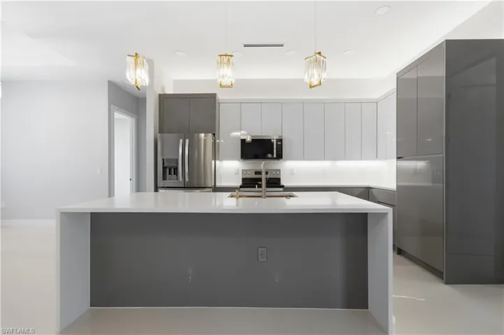 Kitchen featuring modern cabinets, stainless steel appliances, pendant lighting, gray cabinets, and light stone countertops