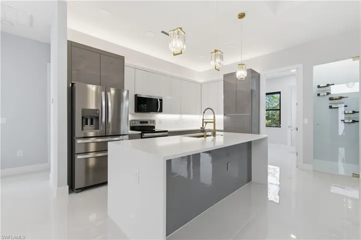 Kitchen with modern cabinets, appliances with stainless steel finishes, pendant lighting, an island with sink, and light stone countertops