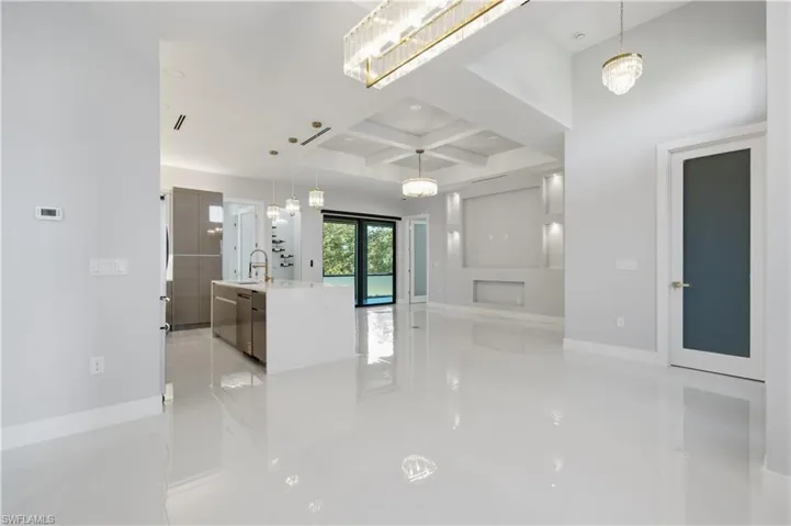 Kitchen with coffered ceiling, a center island with sink, hanging light fixtures, beamed ceiling, and light stone countertops