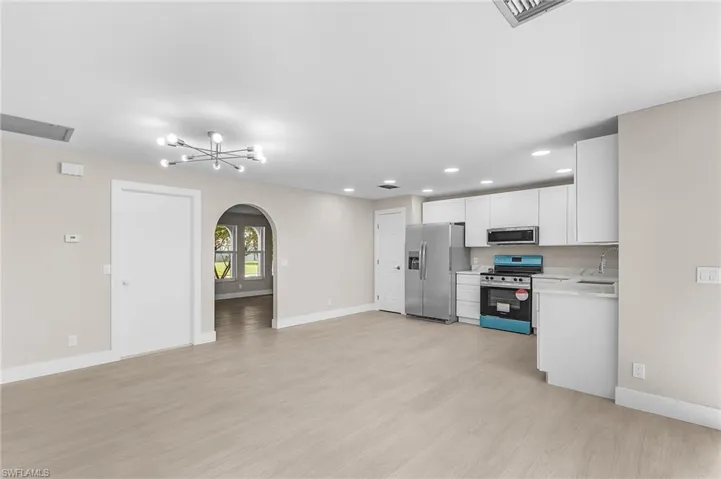 Kitchen featuring arched walkways, white cabinets, appliances with stainless steel finishes, recessed lighting, and light wood-style flooring