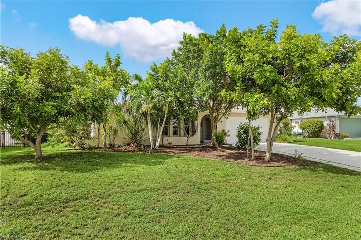View of property hidden behind natural elements featuring a front yard, concrete driveway, stucco siding, and a garage