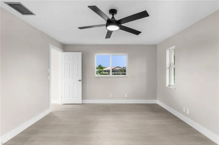 Empty room with light wood-style floors, plenty of natural light, and ceiling fan