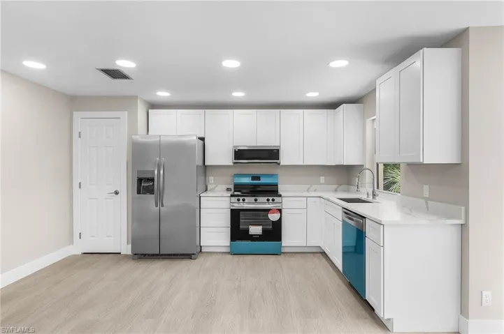 Kitchen featuring stainless steel appliances, white cabinets, light wood-style floors, recessed lighting, and light stone counters