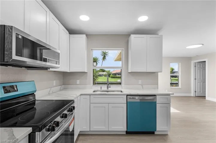 Kitchen featuring appliances with stainless steel finishes, white cabinetry, light stone counters, light wood-style flooring, and recessed lighting