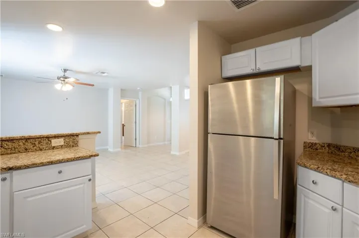 Kitchen featuring white cabinetry, light stone countertops, freestanding refrigerator, light tile patterned floors, and arched walkways