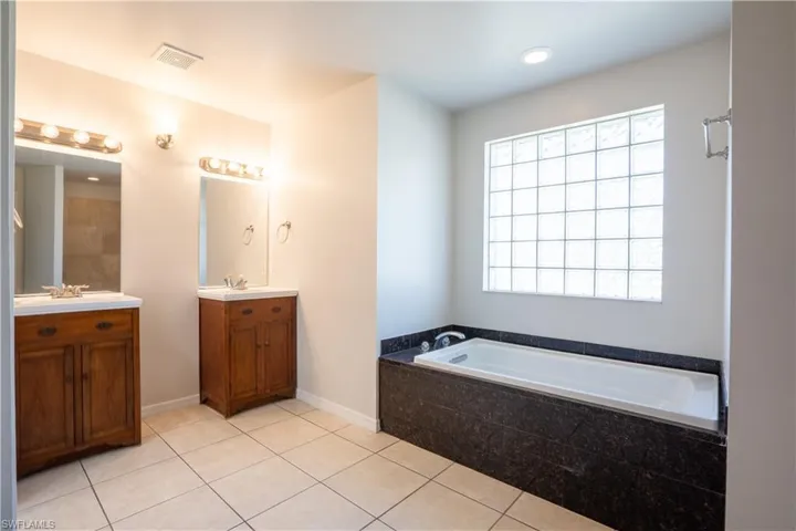 Bathroom with two vanities, a garden tub, light tile patterned floors, and recessed lighting