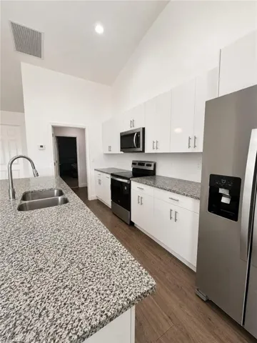 Kitchen featuring white cabinetry, speckled countertops, stainless steel appliances, and wood-finish flooring
