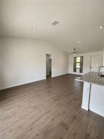 Open-concept living area featuring wood-finish flooring, recessed lighting, vaulted ceilings, and a kitchen island with a stone countertop