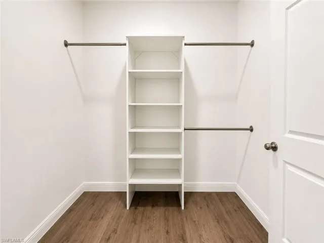 Walk-in closet featuring built-in shelving, two clothing rods, wood-finish flooring, and crisp white walls