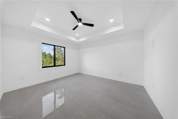 Spacious room featuring a tray ceiling with recessed lighting and a ceiling fan, a large window with black framing, and polished grey tile flooring