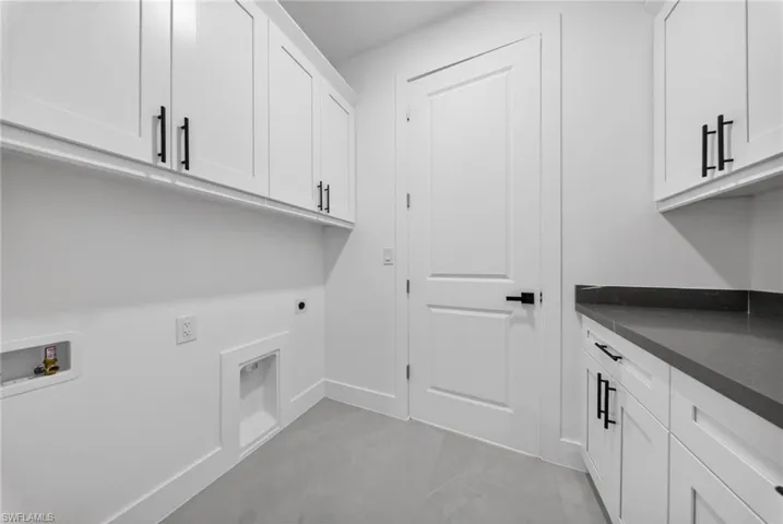 Laundry room featuring extensive white cabinetry, dark countertops, and tile flooring