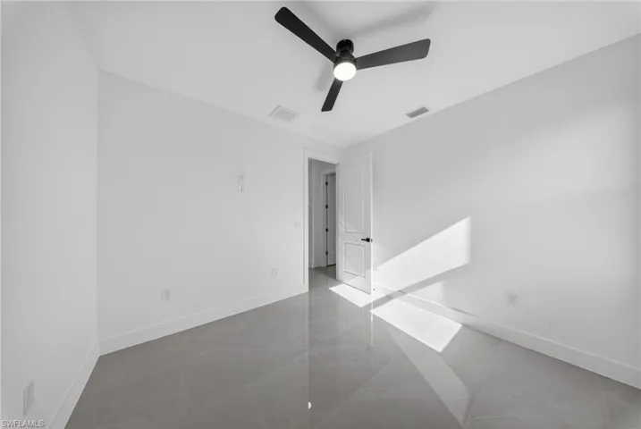 Room featuring large format grey tile flooring, white baseboards, and a black ceiling fan with integrated lighting