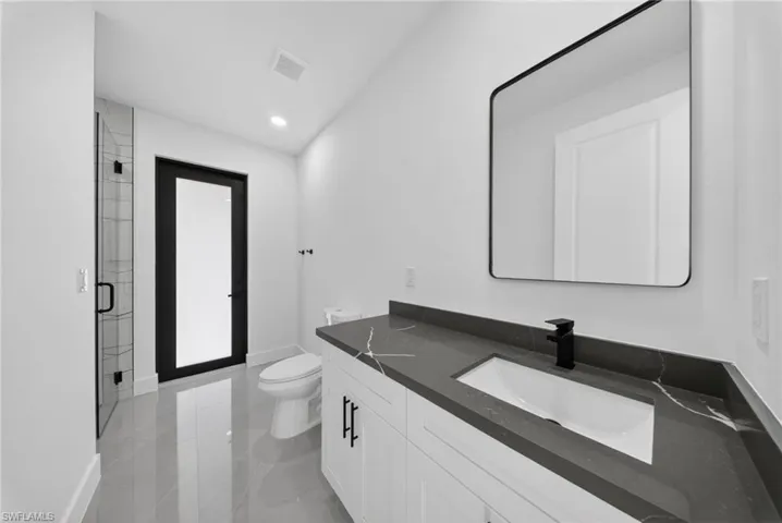 Contemporary bathroom featuring a dark grey countertop with white veining, integrated rectangular sink, and matte black faucet