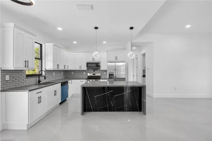 Modern kitchen featuring an expansive center island with a dark stone waterfall countertop, white flat-panel cabinetry with black hardware, an undermount sink with a gooseneck faucet, and stainless steel appliances