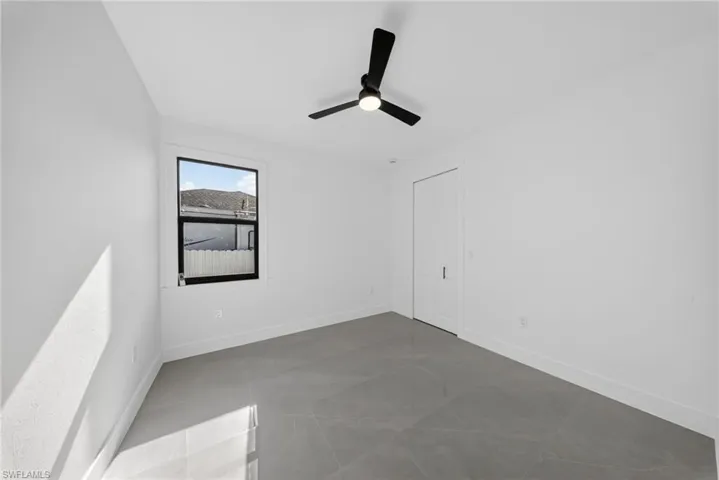 Light-filled room featuring a single window with black trim, a modern black ceiling fan, white walls, and large format grey tile flooring